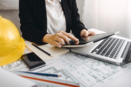 Two colleagues discussing data working and tablet, laptop with on on architectural project at construction site at desk in office
